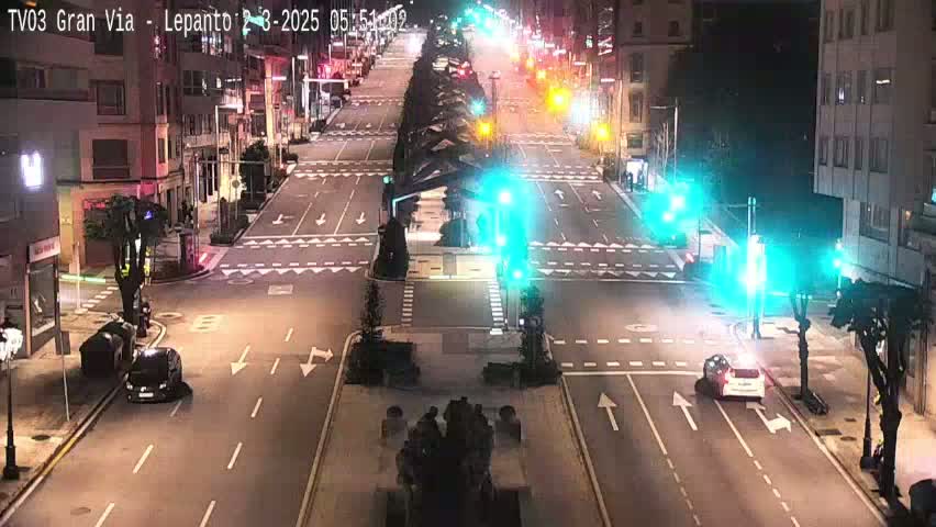 A nighttime, street-level view of a city intersection with several cars and traffic lights, showing light traffic under clear skies.