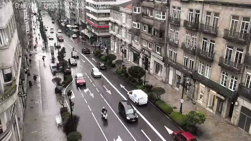 A rain-slicked city street with several cars and pedestrians, flanked by multi-story buildings.
