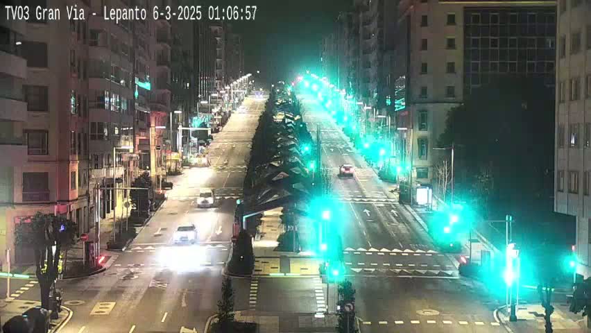 A nighttime, city street scene shows sparsely trafficked roads lined with buildings and streetlights, with some cars visible at intersections.