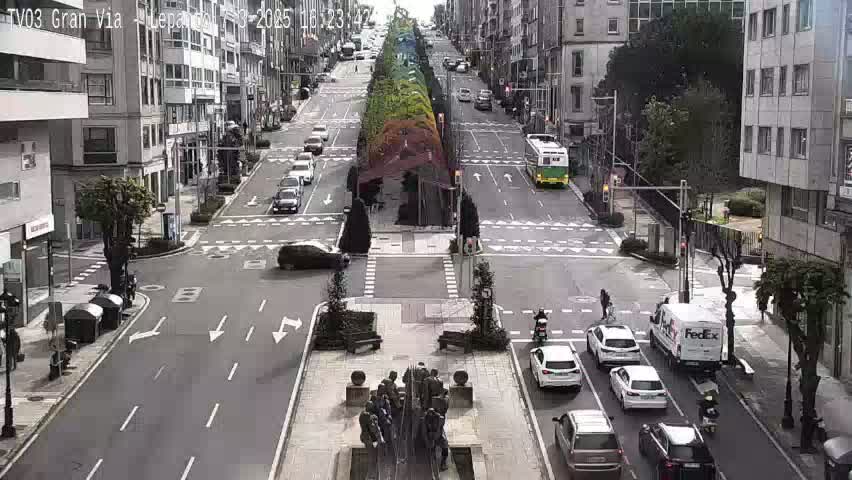 A city street scene on an overcast day shows several cars and a FedEx truck at a crossroads, with a statue in the center of the intersection and multi-story buildings lining the street.