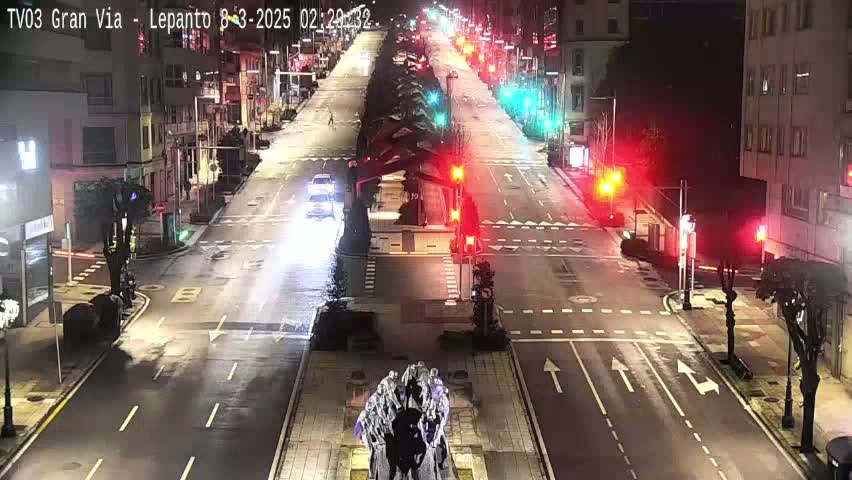 A mostly empty, wet city street at night, with several cars and traffic lights visible.