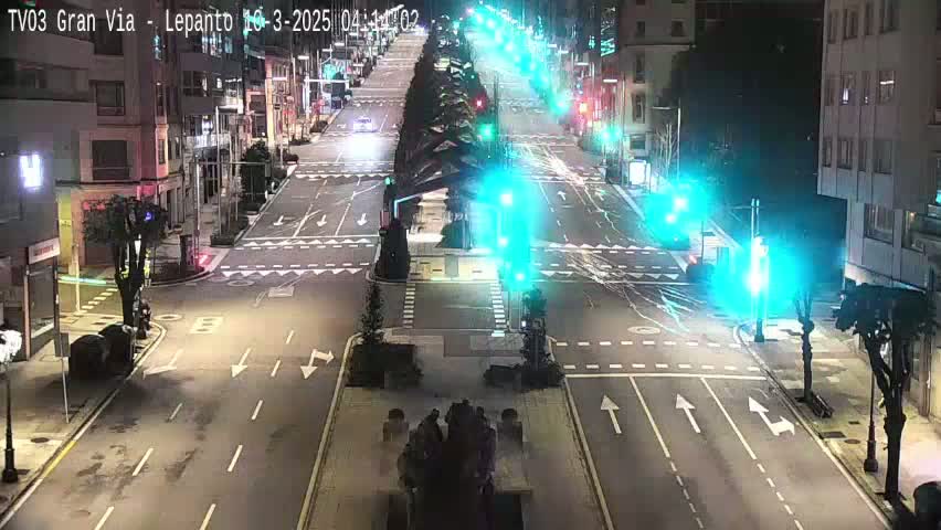 A mostly empty city street at night, illuminated by streetlights and traffic signals, with a few vehicles visible.