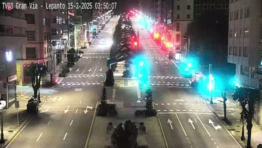 A mostly empty city street at night, illuminated by streetlights, shows intersections with traffic signals and some vehicles are visible in the distance.