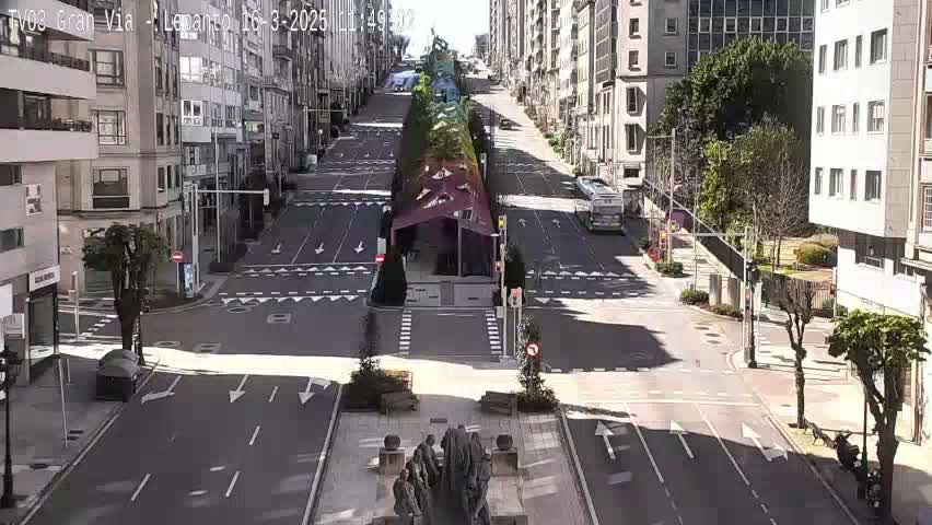 A mostly empty city street on a sunny day, with a large colorful structure in the middle of the road and buildings lining both sides.