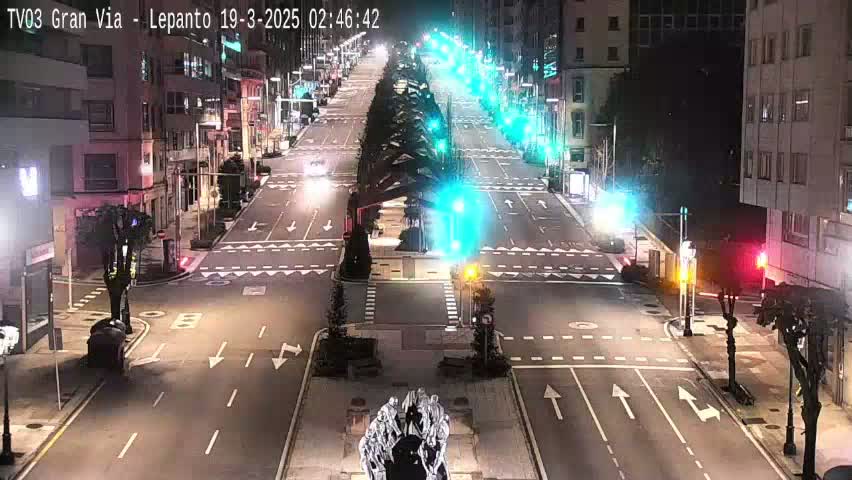 A nighttime, high-angle view of a mostly empty city street intersection with traffic lights and buildings on either side.