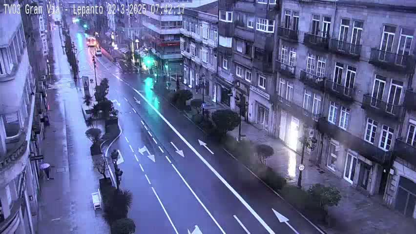 A rain-slicked street scene shows a multi-lane road flanked by tall buildings, with sparse pedestrian and vehicular traffic.