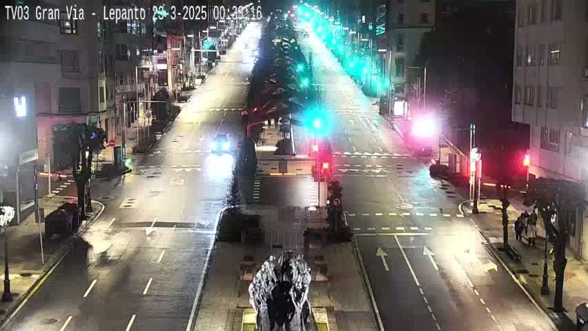 A mostly empty city street at night, with a few cars and pedestrians visible under streetlights.