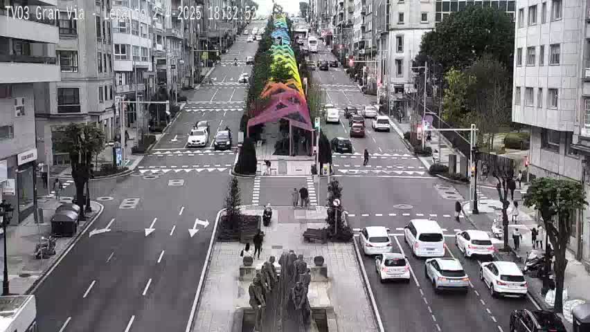 A city street scene with a rainbow-colored canopy overhead, several cars driving, and pedestrians walking on the sidewalks under an overcast sky.