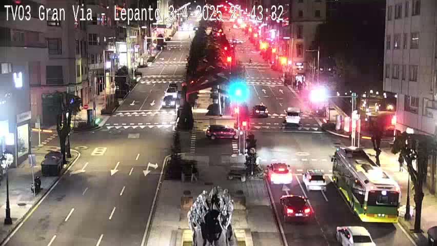 A nighttime view of a city street intersection with several cars and a bus, under clear skies.