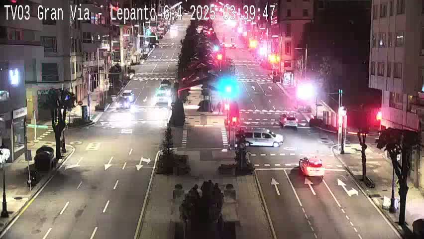 A nighttime, high-angle view of a city intersection with several vehicles moving through it under streetlights.