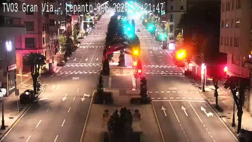 A mostly empty, brightly lit city street at night with traffic lights and a few cars.