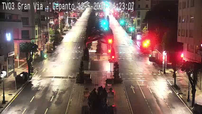 A wet, empty city street at night is illuminated by streetlights and traffic signals.