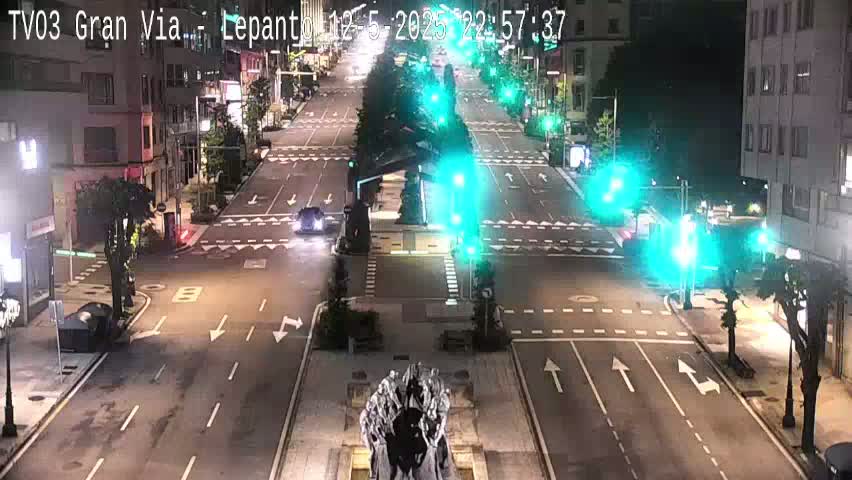 A nighttime view of a city intersection with sparse traffic, illuminated by streetlights and traffic signals.