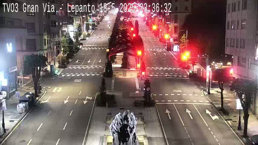 A nighttime, mostly empty city street intersection with traffic lights and a sculpture in the center.