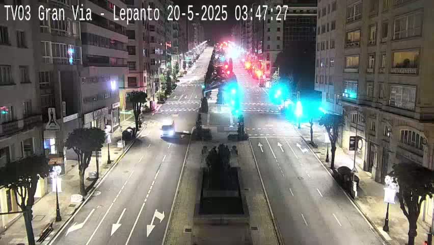 A nighttime street scene shows a wide, multi-lane road with sparse traffic, lined with buildings on both sides, under clear skies.