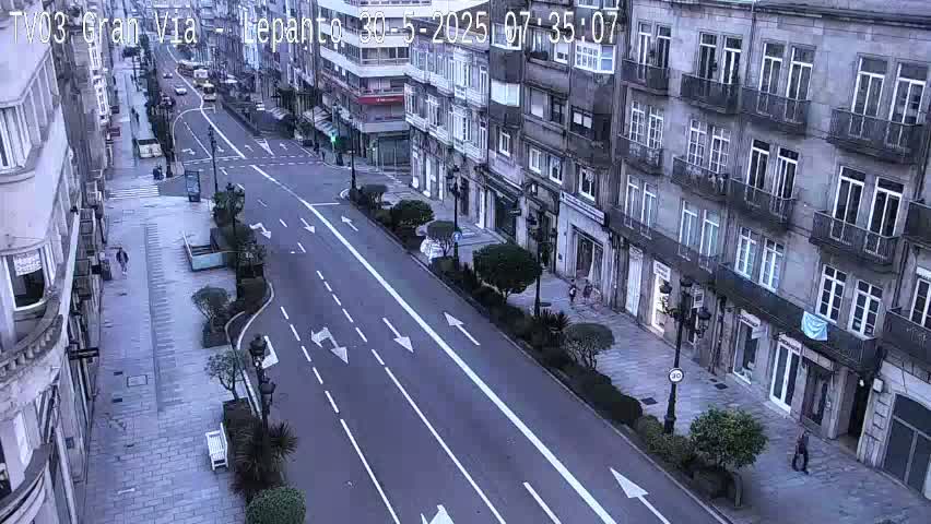 A mostly empty city street with multi-story buildings on either side under a seemingly overcast sky.