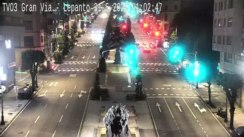 A nighttime, high-angle view of a city intersection with sparse traffic and a central monument.
