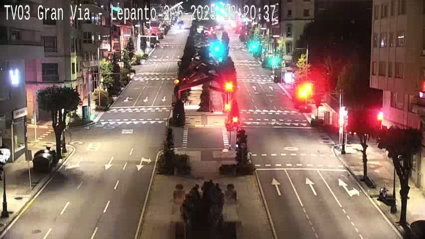 A nighttime view of a mostly empty city intersection with traffic lights and streetlights illuminating the road.