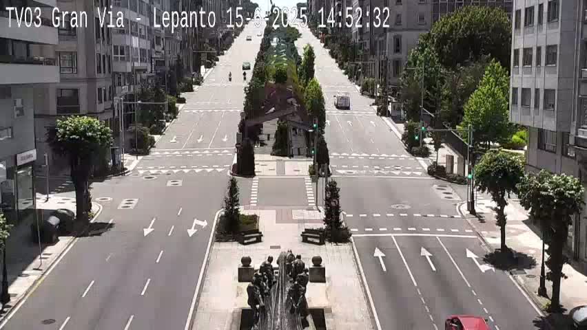 A mostly empty, wide city street on a sunny day, with buildings lining both sides and a central monument.