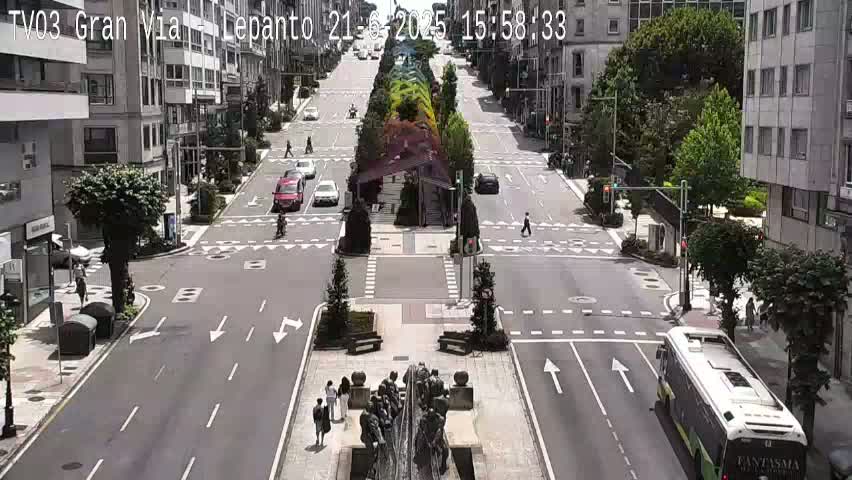 A sunny city street scene shows a wide avenue with cars, pedestrians, and a bus, centered around a large fountain sculpture in a plaza.
