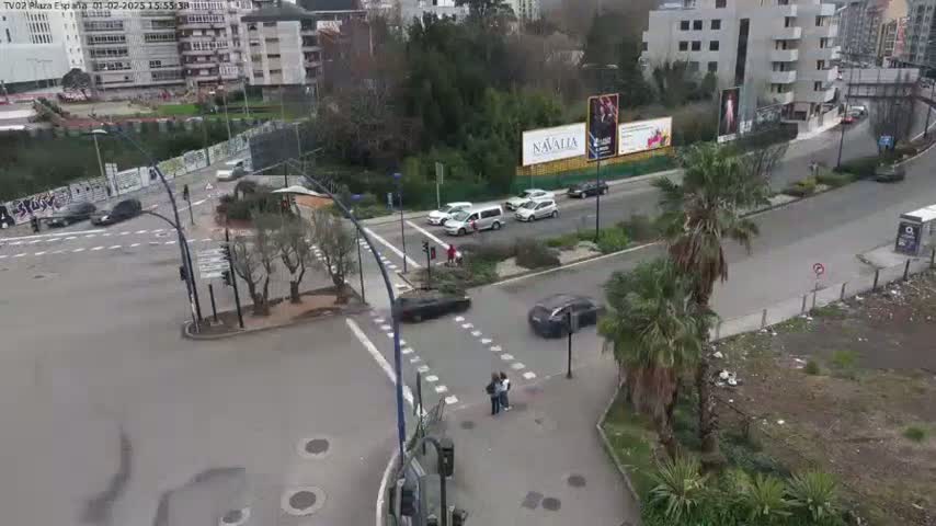 An aerial view shows a multi-lane road intersection with several cars and pedestrians, under an overcast sky.