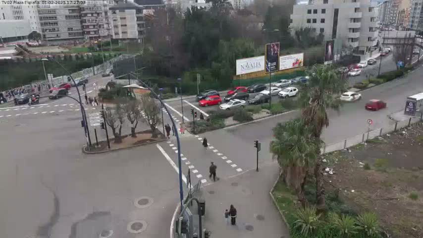 A high-angle view of a city intersection with numerous cars and pedestrians, under an overcast sky.