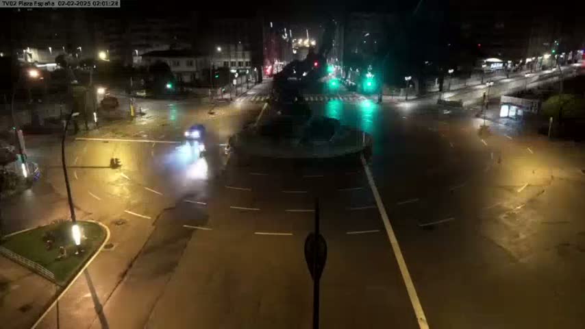 A nighttime view of a flooded city intersection with a few vehicles navigating the waterlogged streets under streetlights.