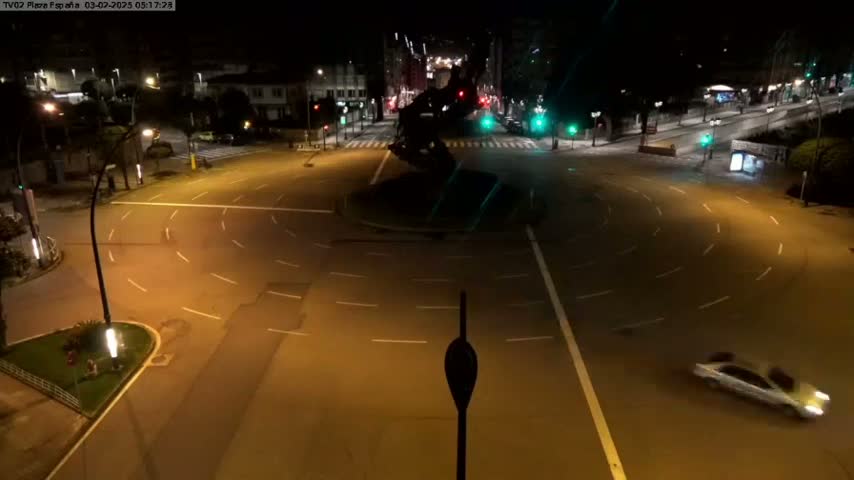 A nighttime aerial view of a circular traffic intersection with a few cars and buildings in the background under clear skies.