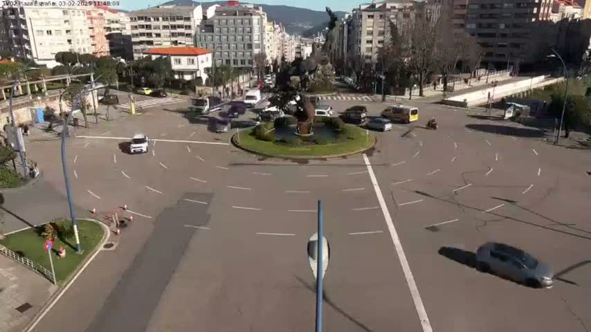 A sunny day reveals a roundabout surrounded by buildings and cars, with a statue at its center.