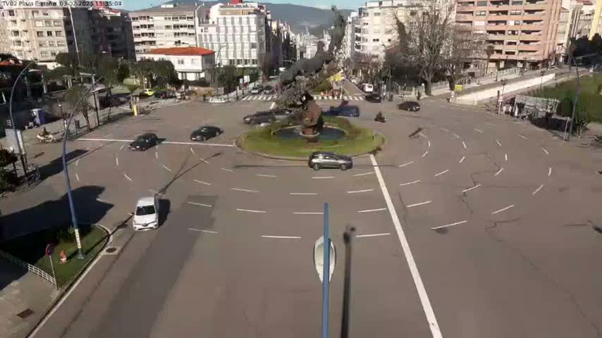A roundabout in a city with several cars driving around it on a sunny day.
