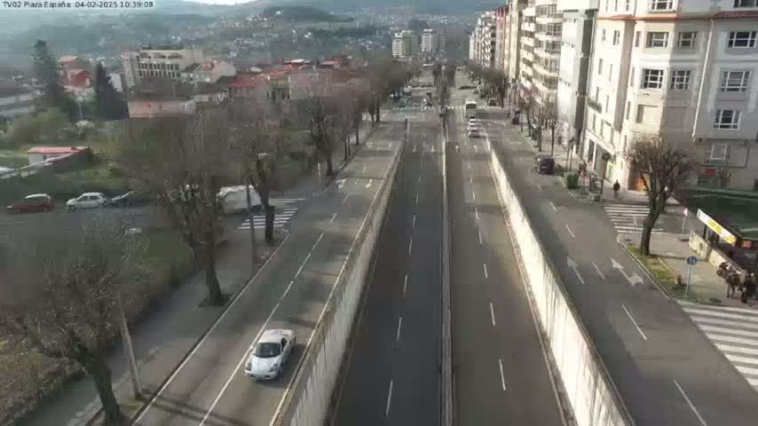 A sunny day reveals a highway cutting through a town, with buildings lining the road and a few cars visible.