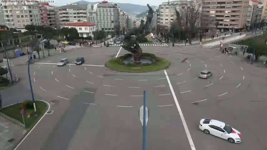 A roundabout with several cars, a large statue in the center, and buildings surrounding it on a partly cloudy day.