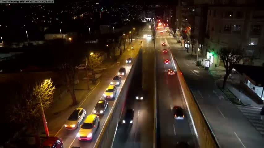 A nighttime aerial view of a multi-lane road with cars driving in both directions, surrounded by buildings and trees.