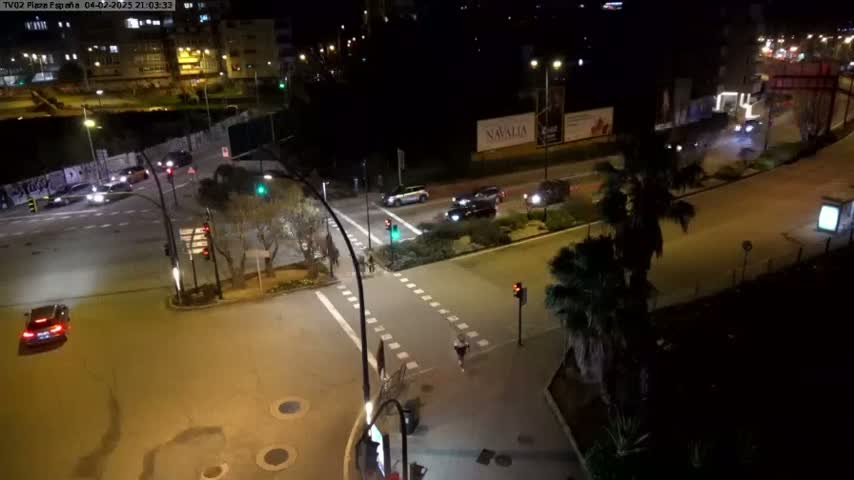 A nighttime aerial view of a street intersection with several cars and pedestrians, illuminated by streetlights.