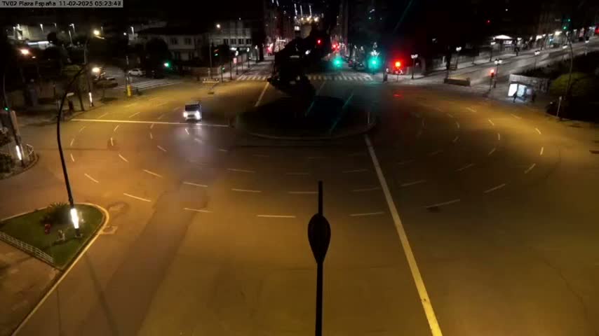 A nighttime overhead view shows a mostly empty roundabout with a few vehicles and streetlights illuminating the surrounding streets.