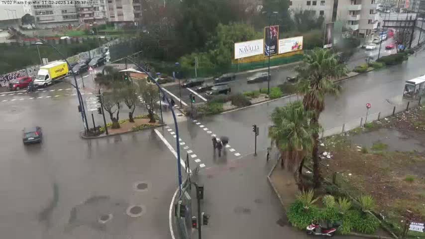 A rain-soaked intersection shows several cars and pedestrians navigating a wet roadway, surrounded by palm trees and buildings.