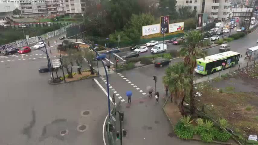 A rainy day scene shows a multi-lane intersection with cars, a bus, pedestrians, and palm trees, near buildings and billboards.