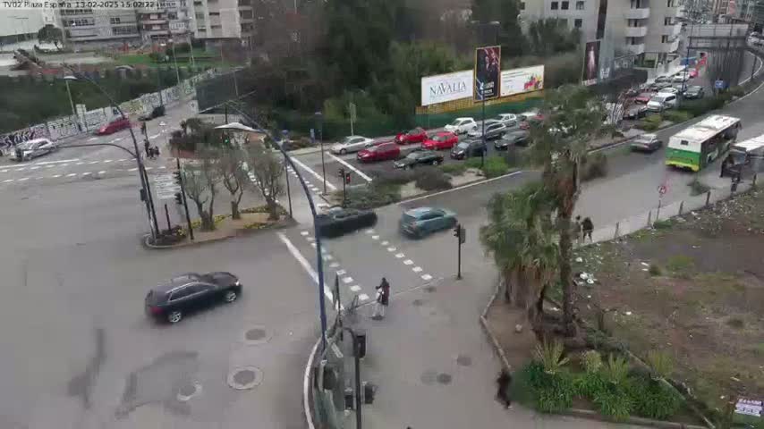 A street intersection with several cars and a bus, surrounded by buildings and trees on an overcast day.