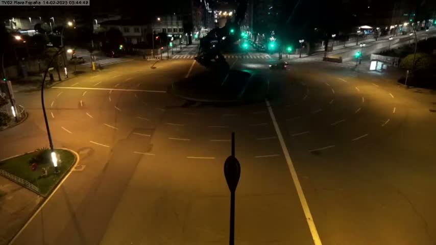 An illuminated roundabout at night with a few vehicles visible on the surrounding roads.