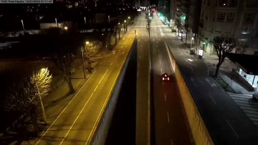 A mostly empty, brightly lit city street at night, with a few cars and bare trees lining the sides.