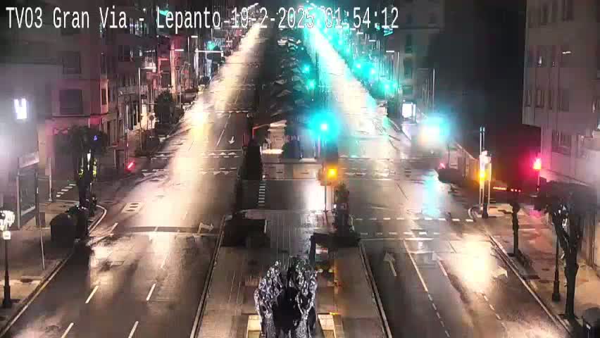 A wet, nighttime street scene shows a city intersection with sparse traffic under streetlights.