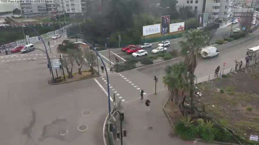 A high-angle view of a city intersection with several cars and pedestrians, on a cloudy day.