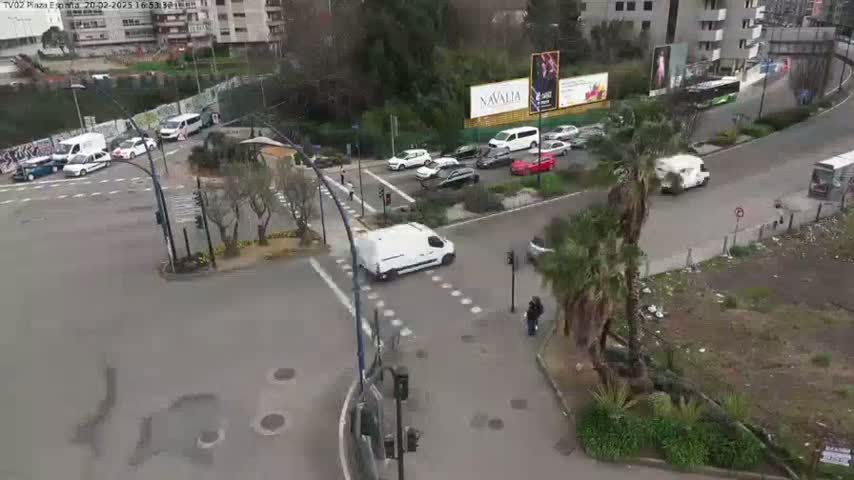 A high-angle view shows a city intersection with several cars and a van, under an overcast sky.