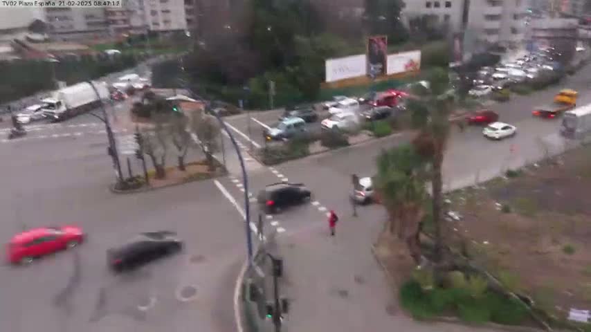 A high-angle view of a busy intersection with several cars and pedestrians, on an overcast day.