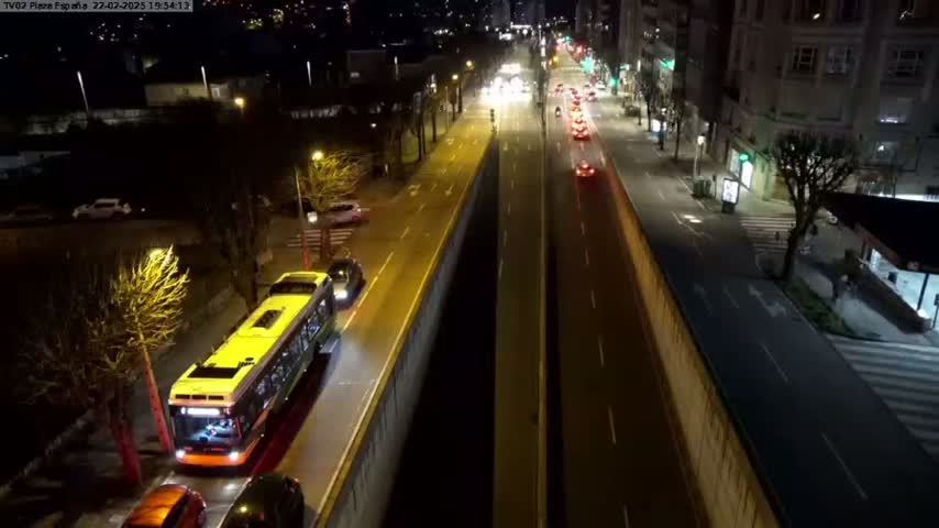 A yellow bus and several cars are traveling along a city street at night.