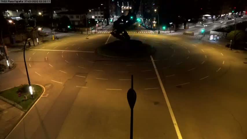 An empty roundabout at night is illuminated by streetlights.
