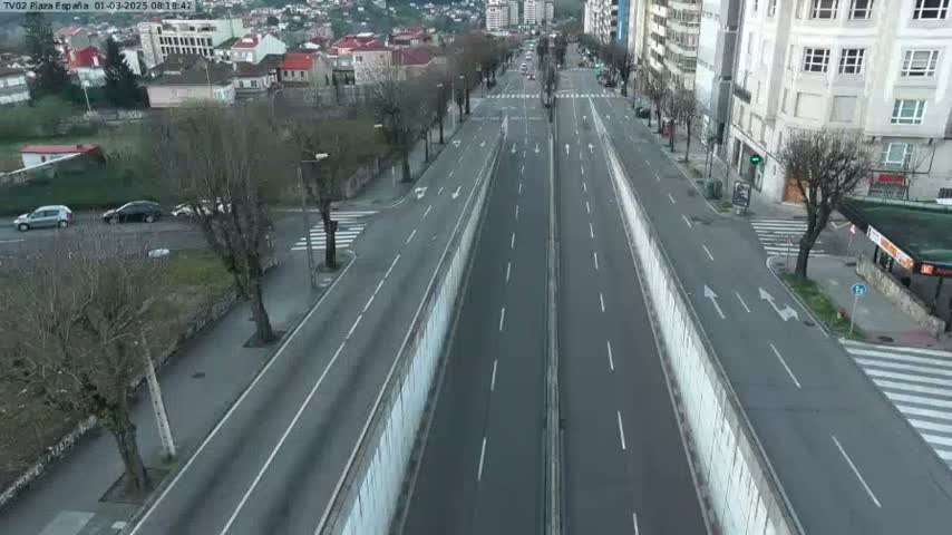 A mostly empty, divided highway cuts through a city, lined with buildings and bare trees under a seemingly overcast sky.