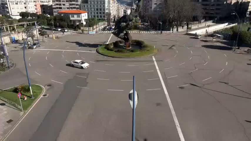 A mostly empty roundabout with a sculpture in the center is shown on a sunny day.