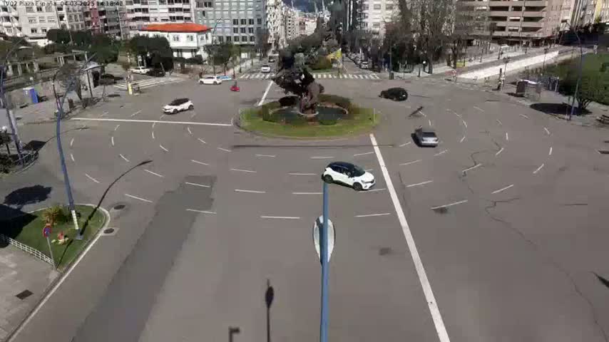 A mostly empty roundabout with several cars and a large statue in the center, on a sunny day.