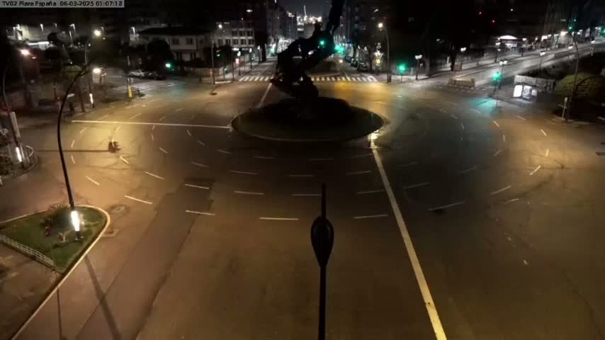 A mostly empty roundabout at night, illuminated by streetlights, with a dark statue in the center.